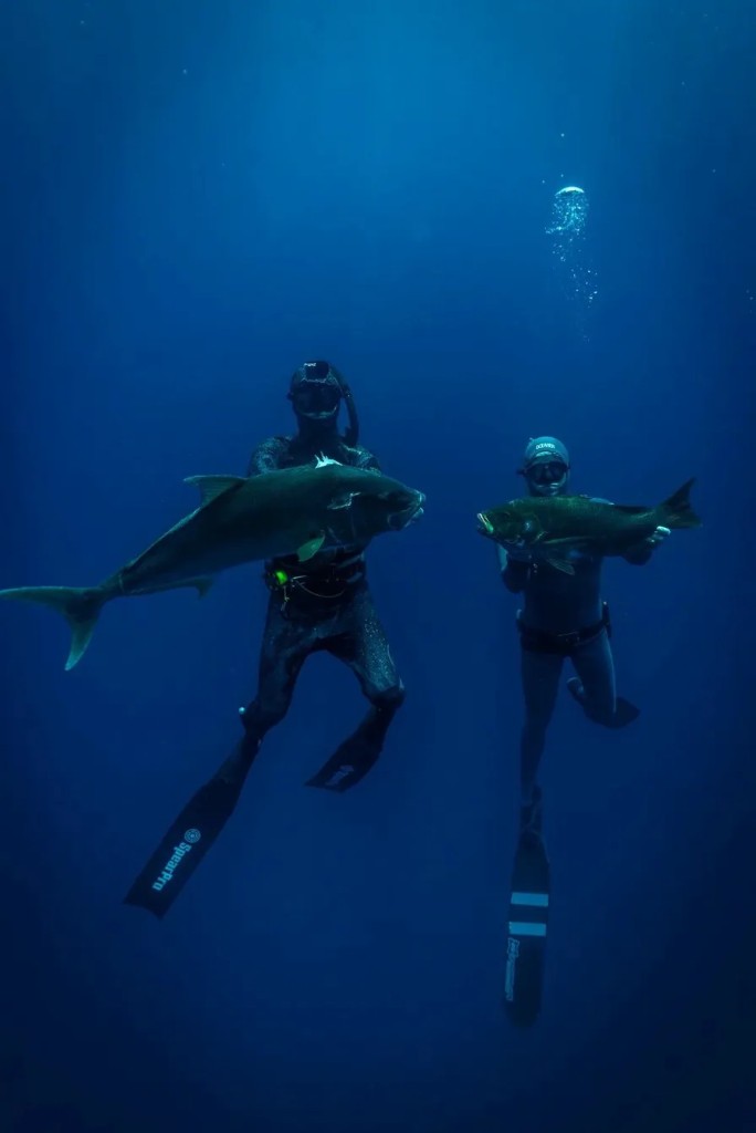Two spearos holding their catch underwater.